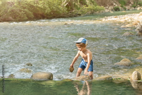 Fototapeta Naklejka Na Ścianę i Meble -  A child builds a small dam of stones in a small mountain river
