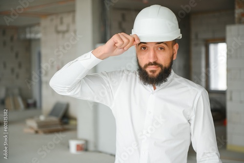 Portrait of good-looking Middle Eastern guy wearing safety helmet and holding construction plan. Employees and business concept.
