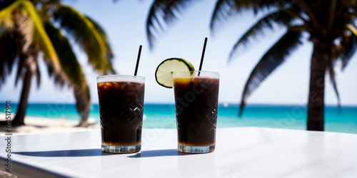 A black cocktail in a glass on a white table against the background of a sea beach on a bright sunny day under palm trees. Generative AI. © Sergiy