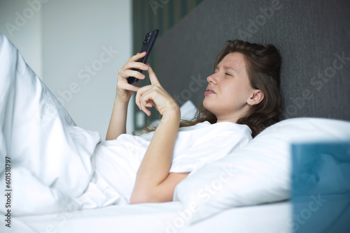 Girl with vision problems tries to read text on the phone. Bad vision concept. Woman looking at the screen of a mobile phone  having vision problems. selective focus in bed in bedroom in the morning 