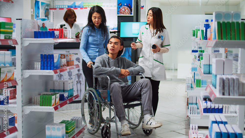 Fototapeta premium Young man wheelchair user talking to pharmacist about medicaments, asking for prescription treatment or medicine. Person with disability and caretaker receiving supplements and vitamins in pharmacy.