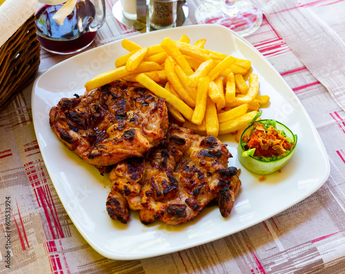 Grilled chicken thighs with garnish of fried potatoes on white plate. Traditional Balkan cuisine, Pileci Batak photo