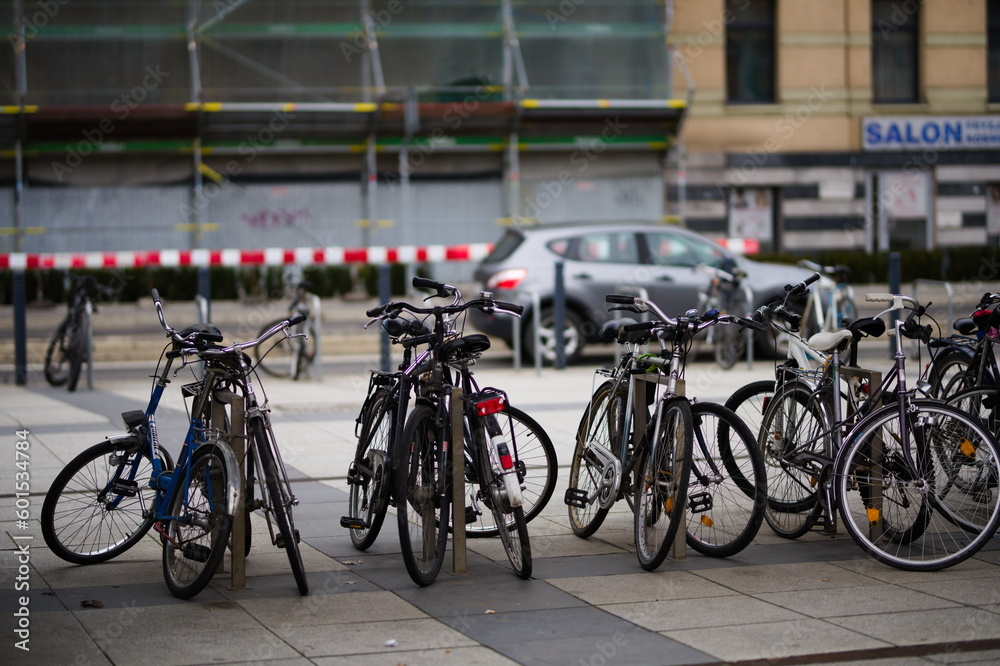 Parking dla rowerów przy miejskiej ulicy z wieloma rowerami przypiętymi do niego, w tle budowa i samochody na ulicy