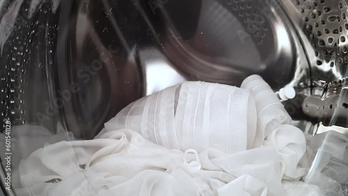 Cleaning white silk curtains in a washing machine with powder. Rotation of an object with a closed door inside.