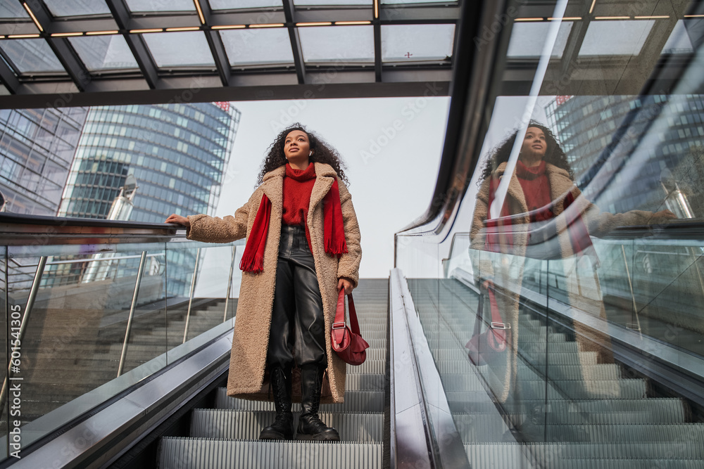 Low angle view of the curly multiracial woman riding down the escalator