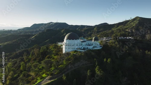 Los Angeles city California USA March 2023. Flying around dome architecture Griffith Observatory, Hollywood sign on bright green hill at sunset. Aerial scenic landmark buildings in green spring park