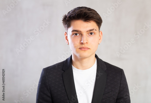 Positive male student in black jacket poses with folded arms on chest on gray background. Guy roustabout crossed his arms