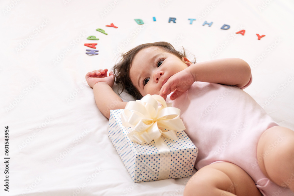 Innocence asian toddler lying down with white gift ribbon box character happy birthday looking to parent on bed at home.Happiness Little daughter received gift box birthday one year growth family care Innocence asian toddler lying down with white gift ribbon box character happy birthday looking to parent on bed at home.Happiness Little daughter received gift box birthday one year growth family care