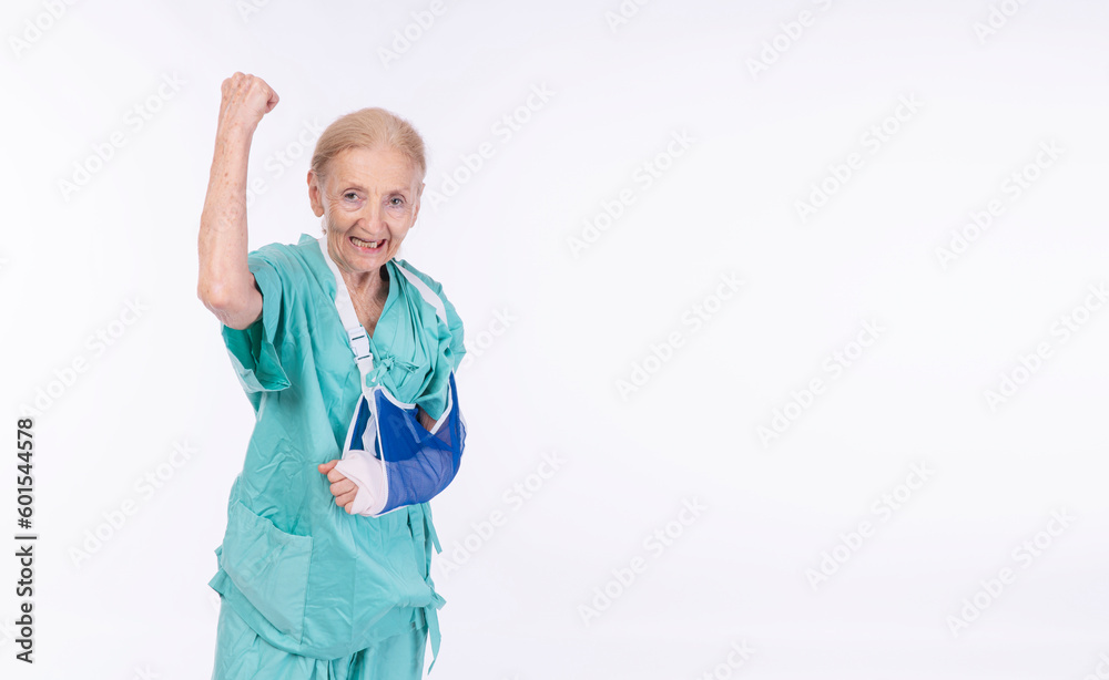 Elderly woman accident broken bone arm wear safety soft splint raised fist standing over isolated white background. Cheerful injured fracture elderly painful bandage arm Insurance accident health care Elderly woman accident broken bone arm wear safety soft splint raised fist standing over isolated white background. Cheerful injured fracture elderly painful bandage arm Insurance accident health care