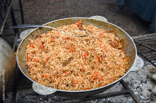 Big cauldron of asian traditional pilaf. Cooking pilaf dish with rice, meat, carrot and spice in outdoor. Street food