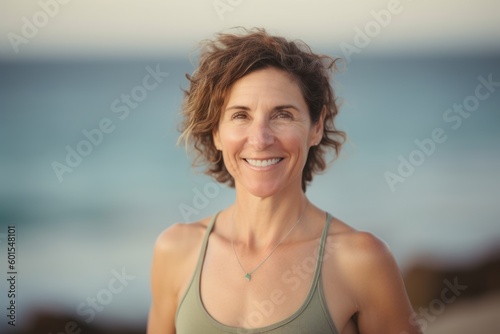 Portrait of smiling woman standing on beach with hands in hair looking at camera