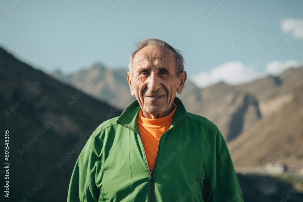 Portrait of a senior man in a green jacket on the background of mountains