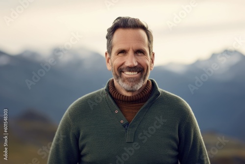 Handsome middle-aged man in a green sweater smiling and looking at the camera in the mountains