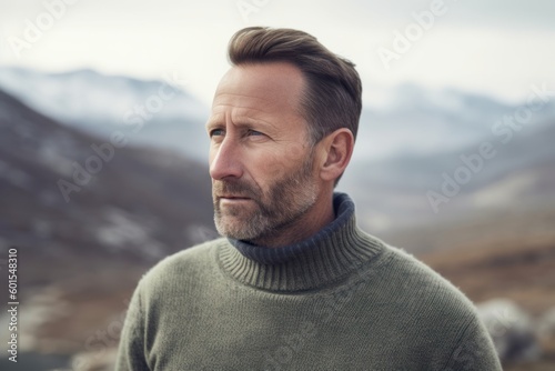 Portrait of a handsome middle-aged man in a knitted sweater against the background of mountains.