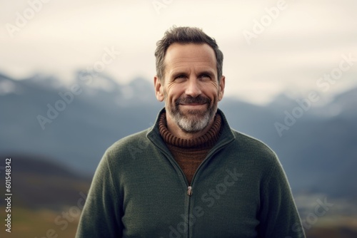 Portrait of a handsome middle-aged man with a beard and mustache, wearing a green sweater, looking at the camera with a smile.