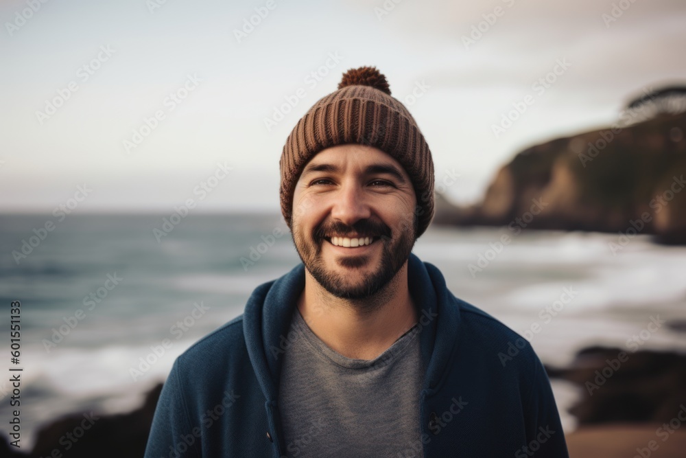 Portrait of a handsome young man in a hat and sweater smiling on the beach