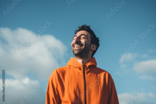 Portrait of a young man in an orange jacket against the sky.