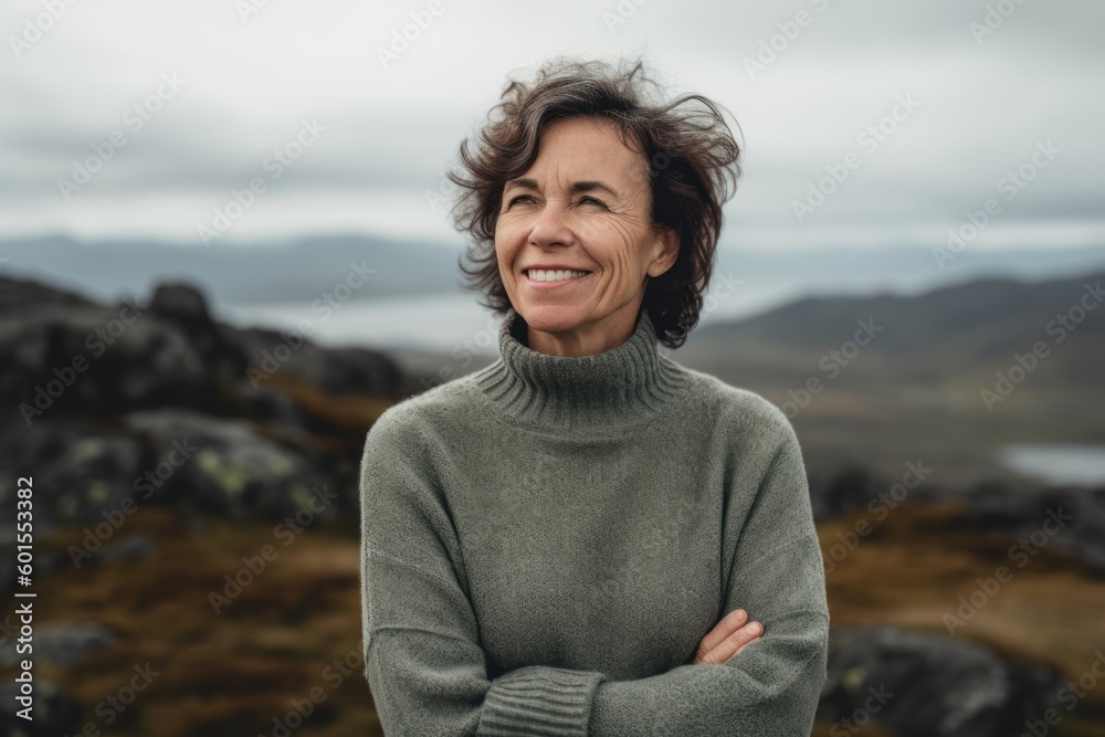 Portrait of smiling senior woman standing with arms crossed on top of mountain