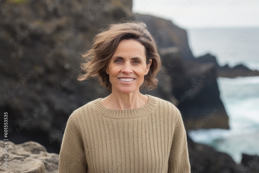 Portrait of smiling middle aged woman standing on rock by the ocean Portrait of smiling middle aged woman standing on rock by the ocean