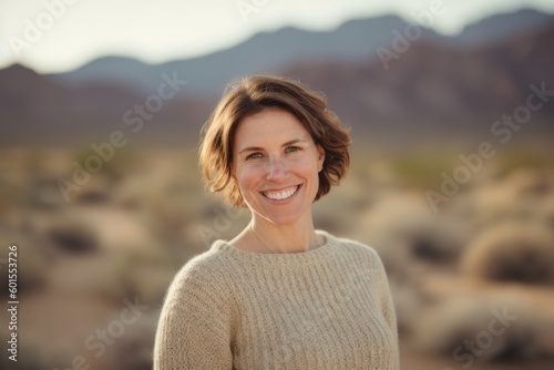 Environmental portrait photography of a grinning woman in her 30s wearing a cozy sweater against a desert background. Generative AI