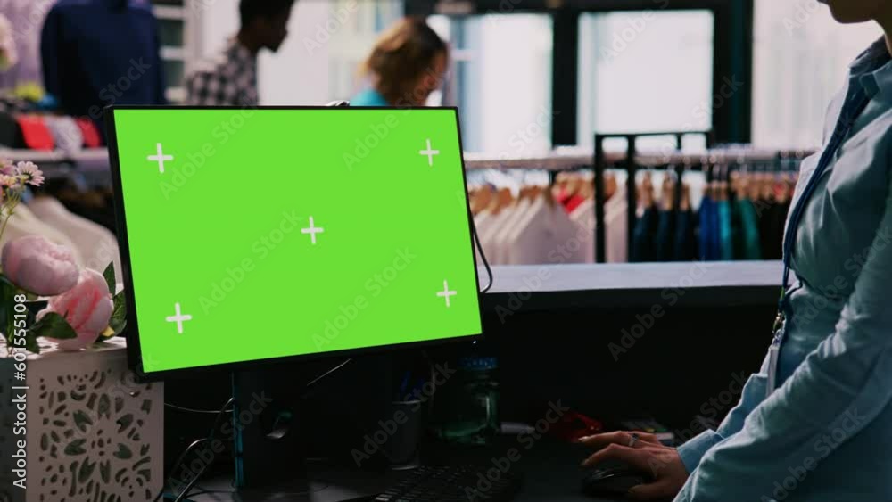 Worker checking computer with chroma key green screen mock up display, standing at counter desk in shopping centre. Manager waiting for customers in modern boutique. Fashion concept Worker checking computer with chroma key green screen mock up display, standing at counter desk in shopping centre. Manager waiting for customers in modern boutique. Fashion concept