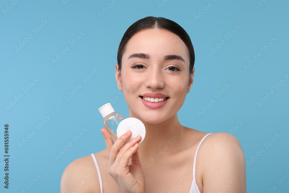 Beautiful woman with makeup remover and cotton pad on light blue background Beautiful woman with makeup remover and cotton pad on light blue background