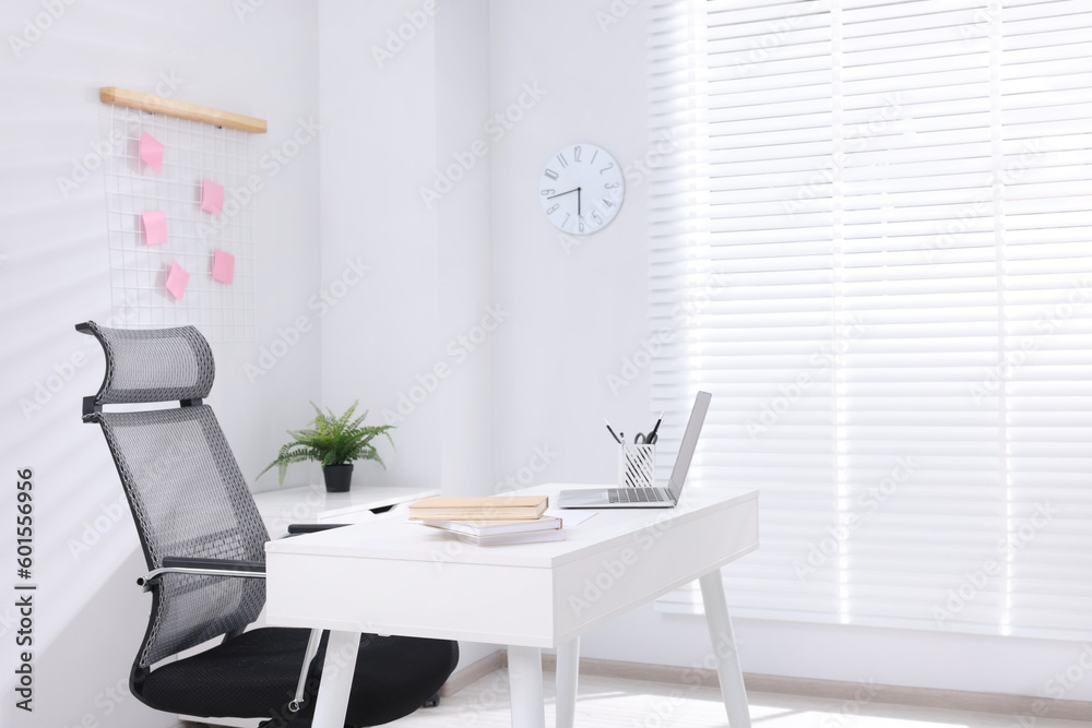 Desk and comfortable chair in modern office, space for text. Interior design