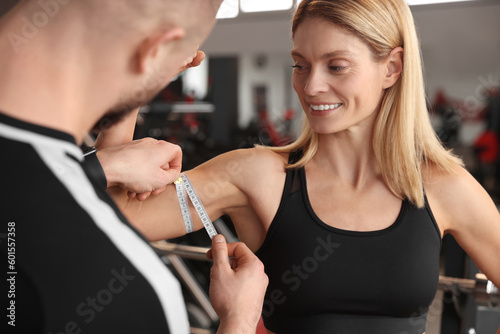 Trainer measuring woman`s biceps with tape in gym