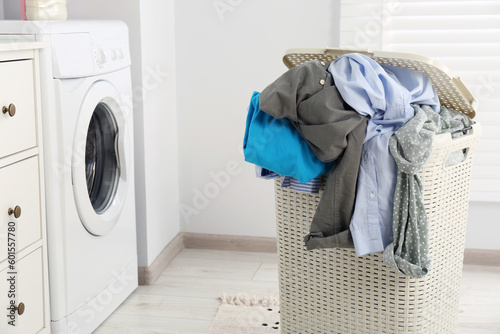 Plastic laundry basket overfilled with clothes in bathroom