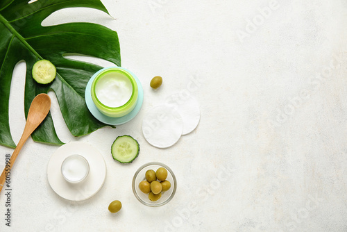 Composition with jars of natural cream, ingredients, cotton pads and palm leaf on light background