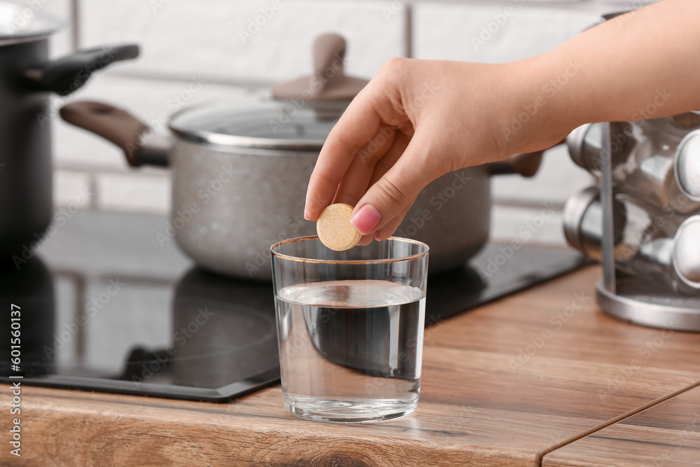 Woman putting effervescent tablet into glass of water on kitchen counter, closeup