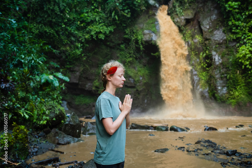 The girl is meditating  her hands are folded in namaste  in the jungle against the backdrop of a waterfall.