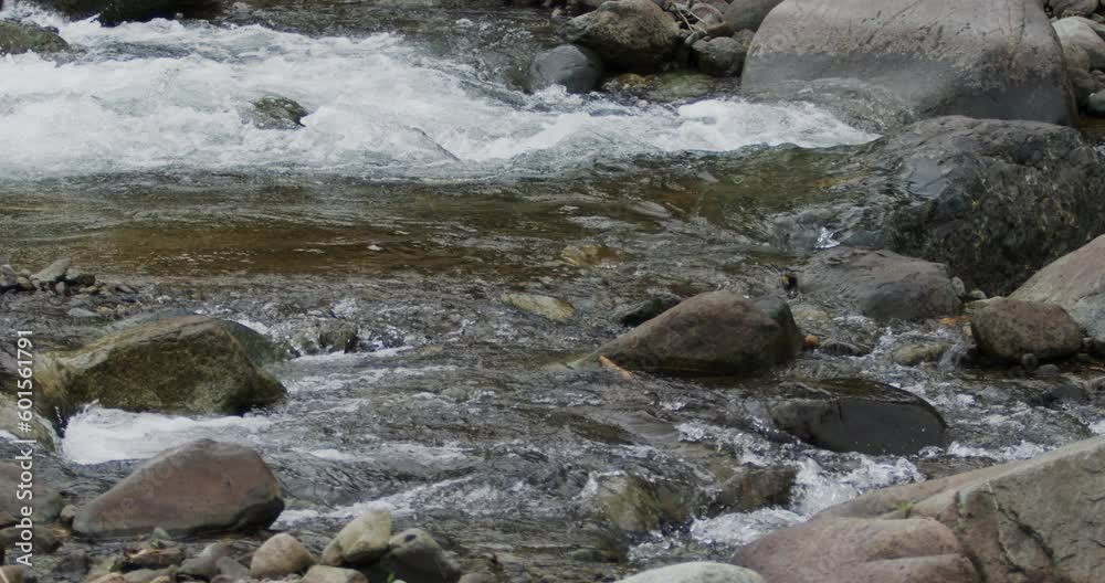 Close up detail of river water current flowing through river rocks in slow motion Close up detail of river water current flowing through river rocks in slow motion