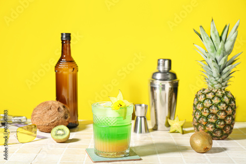Fresh summer cocktail with carambola on tile table near yellow wall