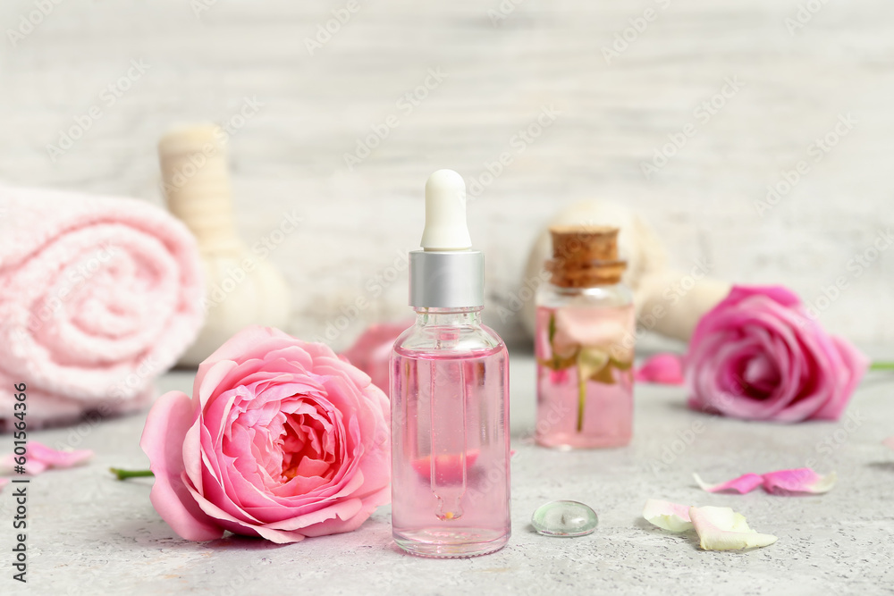 Bottles of cosmetic oil with rose extract and flowers on white table Bottles of cosmetic oil with rose extract and flowers on white table