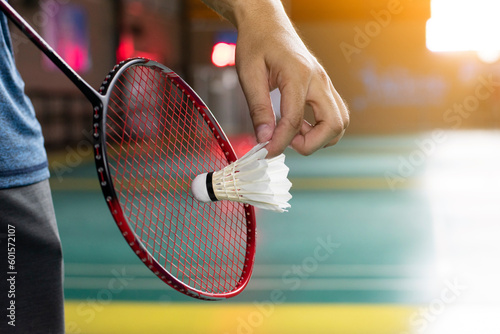 Badminton player is holding white badminton shuttlecock and badminton racket in front of the net before serving it over the net to another side of badminton court. Selective focus on white shuttlecock © Sophon_Nawit