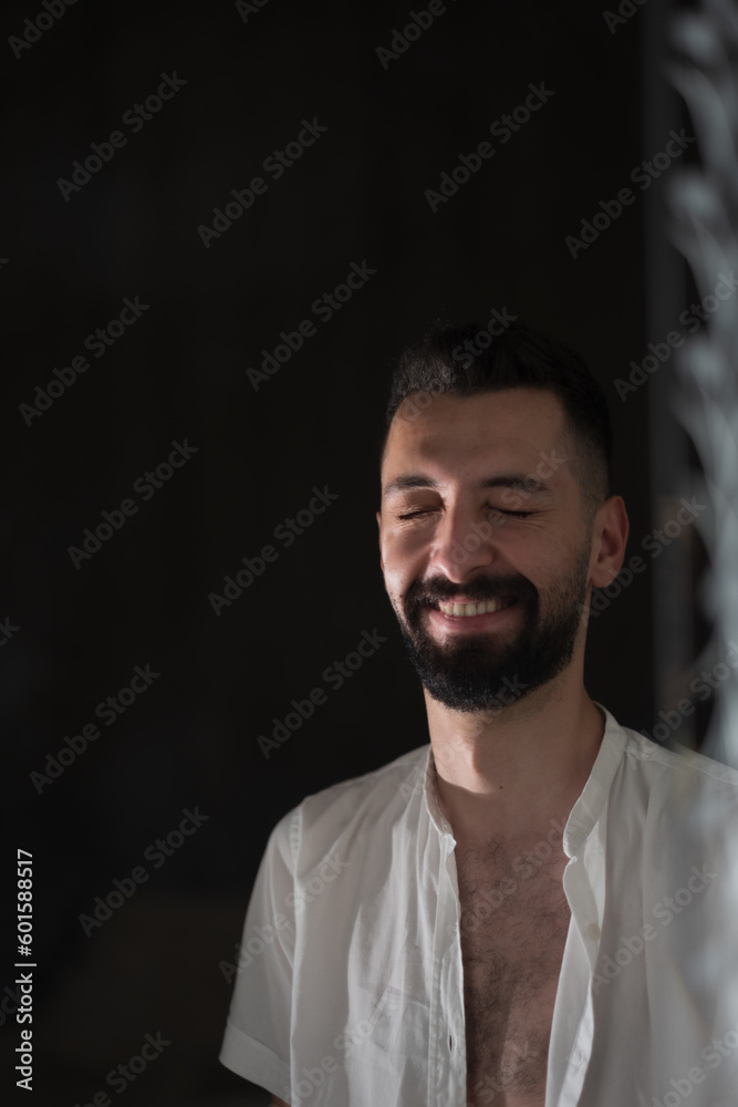 Fototapeta premium A young man with an open shirt laughs cheerfully. A single light illuminates his face.