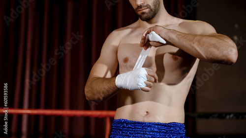 Obraz na płótnie Male boxer with burly figure muscular bearded American preparing for boxing practice Bandage fingers to prevent injuries