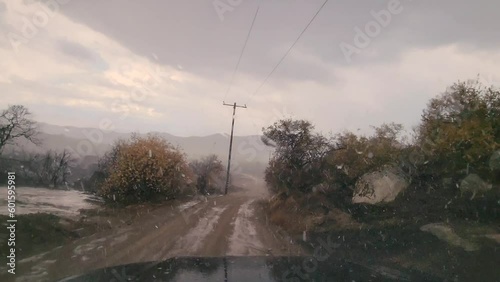 Footage through the windshield of a car driving on a dirt road during snowfall. photo