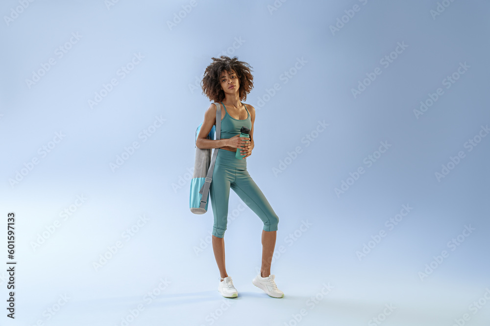 Smiling sporty woman with sports bag and bottle of water after training on studio background Smiling sporty woman with sports bag and bottle of water after training on studio background