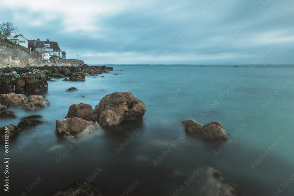 A long exposure shot of the calm blue sea on a rocky shore