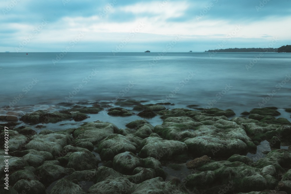 A long exposure shot of the calm blue sea on a rocky shore
