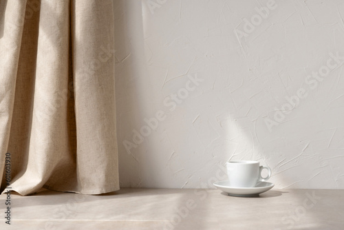 Aesthetic minimalist neutral home interior background, empty white wall, beige linen curtain, stone tabletop, coffee cup in sun light rays