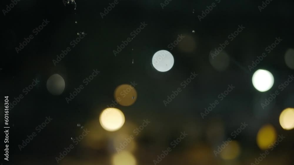 Water droplets from above spin and fall in front of blurry bokeh lights