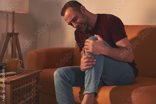 Man with knee pain sitting on a sofa at home.