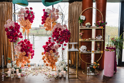Delicious wedding reception luxury ceremony. Background decor. Candy bar. Table with sweets  candies  dessert. Arch  wall decorated pink  orange flowers roses for birthday party in banquet area  hall.