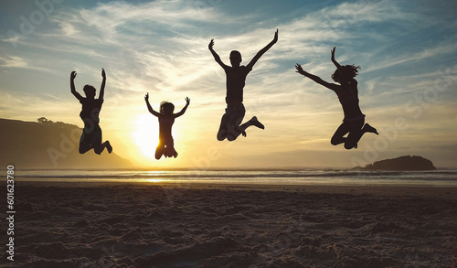 Silhouettes of happy unrecognizable children jumping in the beach at sunset
