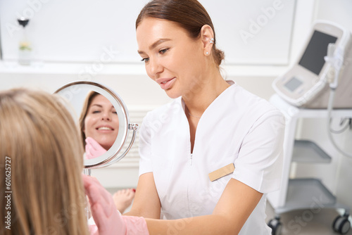 Female cosmetologist at the workplace consults female patient in bathrobe