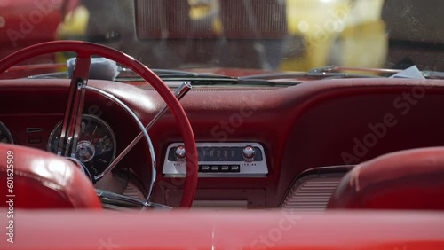 Retro dashboard of old vintage convertible with radio and red leather interior and shiny chrome details. Opposite cabriolet is yellow modern muscle car on sunny day. Near cars walk people.