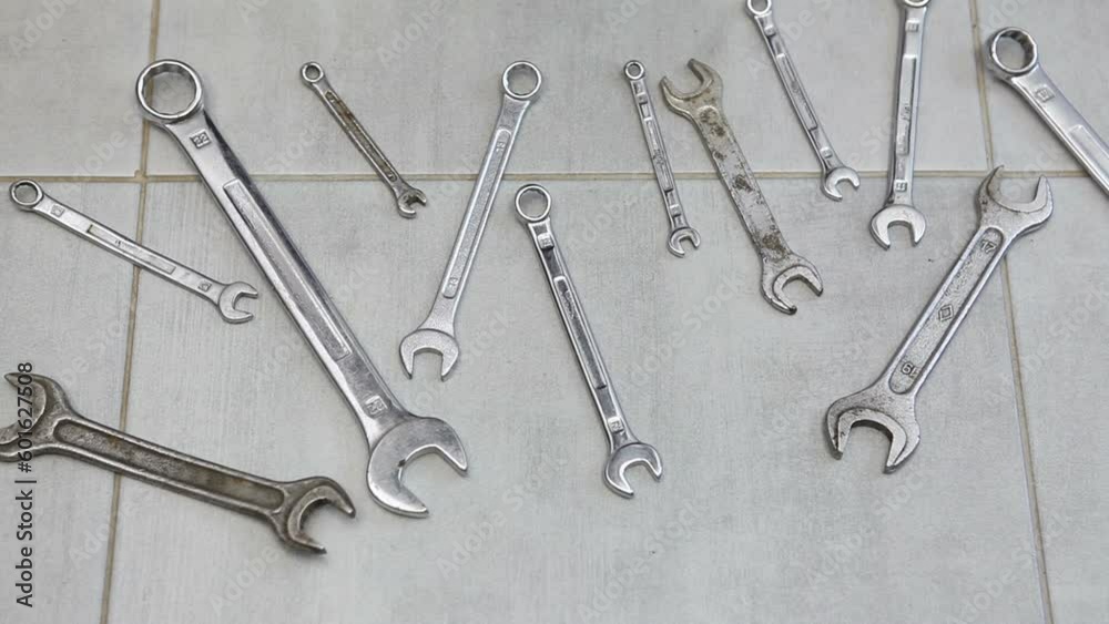 Open-end wrenches and box wrenches of various sizes lie on the ceramic floor. A man picks up wrenches from the floor. Open-end wrenches and box wrenches of various sizes lie on the ceramic floor. A man picks up wrenches from the floor.